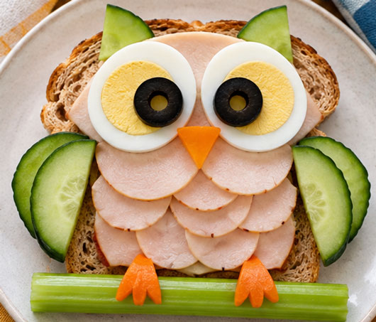 Open-face owl sandwich decorated with eggs, olives and deli meat